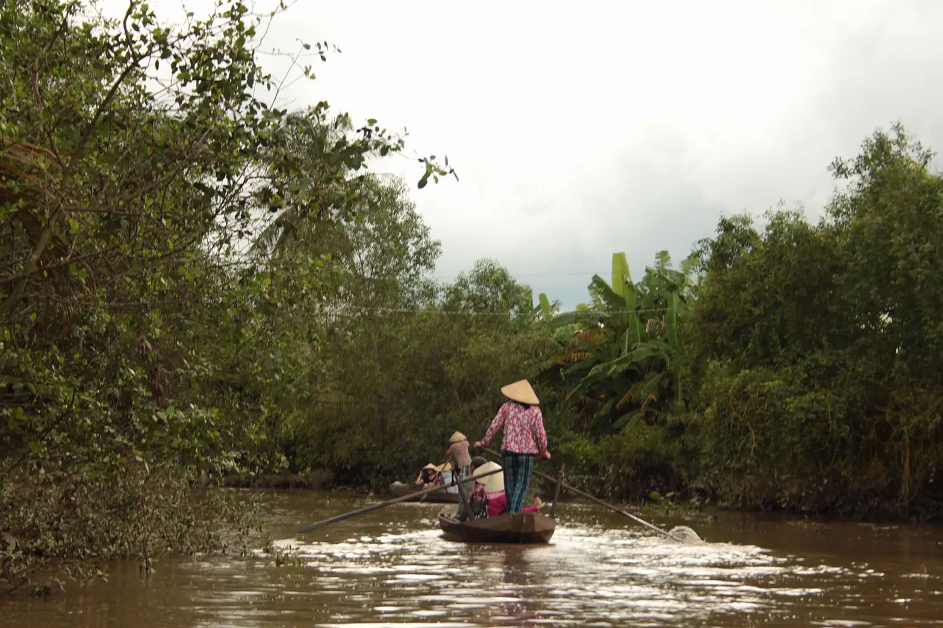 Kobieta w stożkowym kapeluszu steruje łodzią sampan na kanale delty Mekongu w Wietnamie