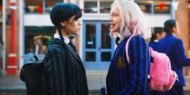 Wednesday in Dark Clothing and Enid in Brighter Clothing Talking to Each Other in Wednesday
