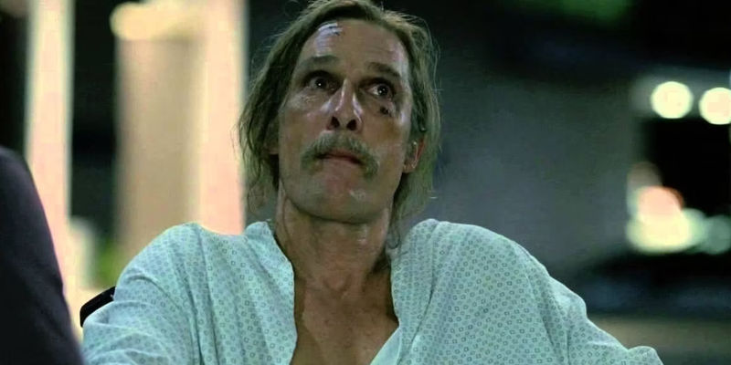 Matthew McConaughey as Rust Cohle with long hair and mustache, wearing a hospital gown, in True Detective season 1 episode 8