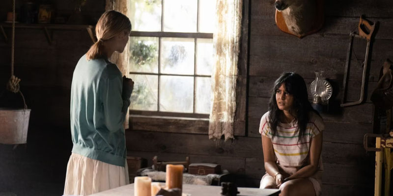 Lottie (Courtney Eaton) sitting in a cabin looking at Laura Lee (Jane Widdop) standing over her in Yellowjackets season 1 episode 6 Saints.