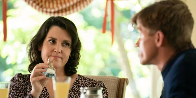 Shauna (Melanie Lynskey) raising a salt shaker to a man at a table in Yellowjackets season 1 episode 6 Saints.