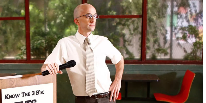 Dean Pelton (Jim Rash) holds a microphone in the cafeteria in Community