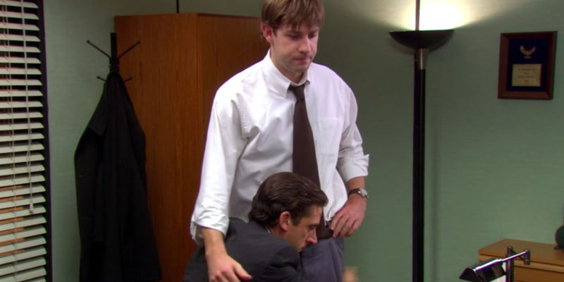 Steve Carell as Michael Scott hugging John Krasinski as Jim Halpert around the waist in The Office