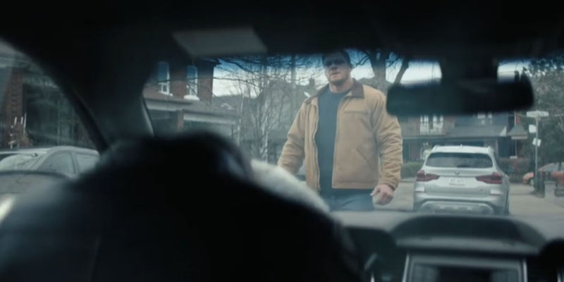 Alan Ritchson as Reacher looking in through a car's front window just after he's kicked the bonnet hard enough to deploy the airbag