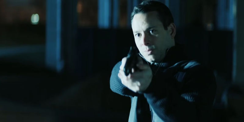 Mishka Thébaud as Grant in Reacher aiming a gun and being lit from the side as a speeding car approaches