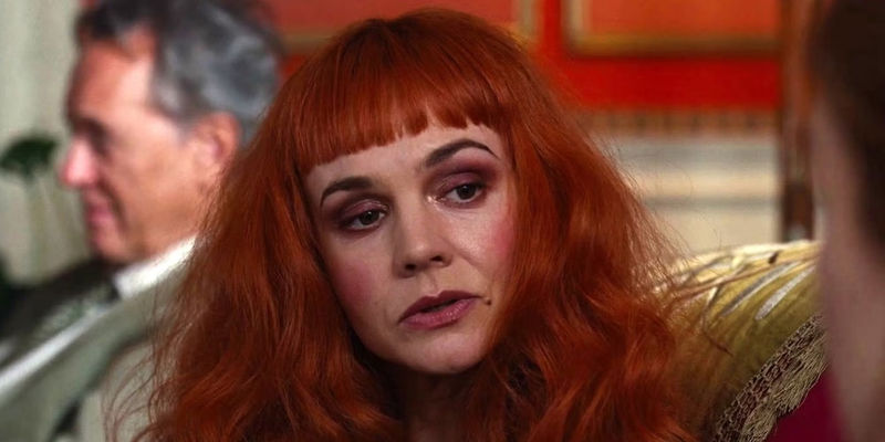 Carey Mulligan as Pamela sitting on a couch in Saltburn