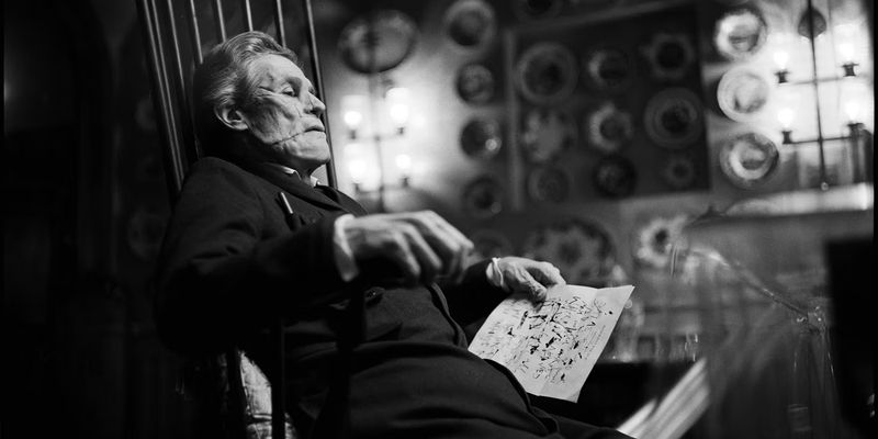 Deformed Willem Dafoe sitting on a chair in Poor Things