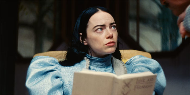 Emma Stone as Bella Baxter / Victoria Blessington holds a book in her hands in a scene from Poor Things.