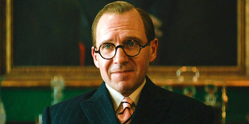 Ralph Fiennes wearing glasses and softly smiling in The King's Man