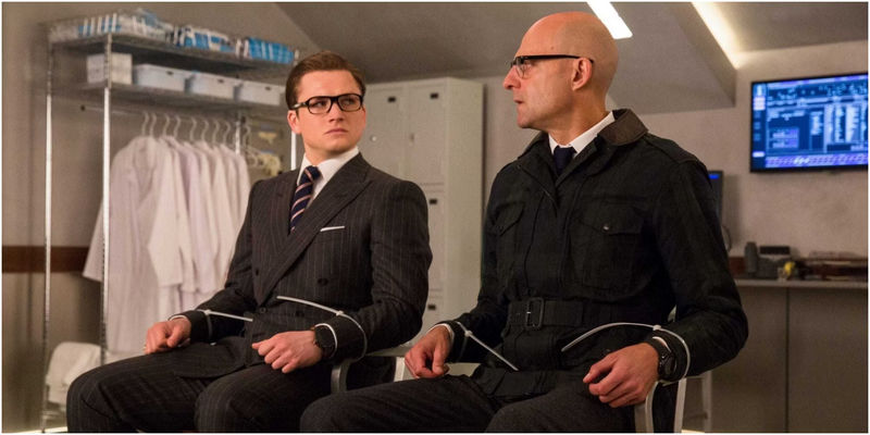 Eggsy and Merlin in suits tied in chairs