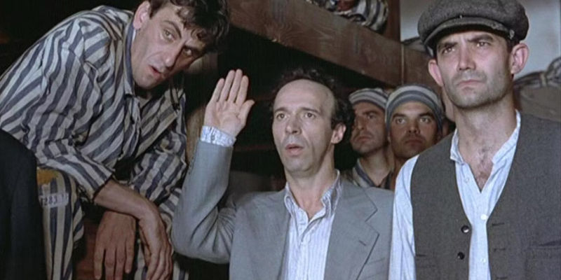 Roberto Benigni as Guido Orefice raising his hand with other men around him at a concentration camp in Life is Beautiful.
