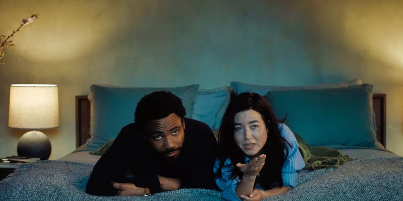Donald Glover and Maya Erskine watching TV in Mr. & Mrs. Smith