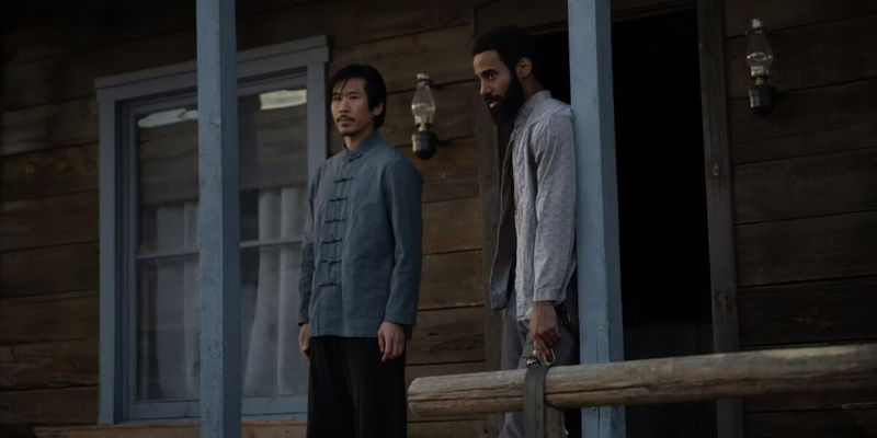 Gus (Philemon Chambers) and Kai (Lawrence Kao) standing on a porch with guns in Walker Independence.
