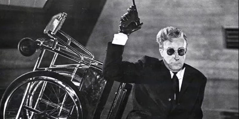 Peter Sellers as Dr. Strangelove sitting beside his wheelchair waving a pistol in the air in Dr. Strangelove