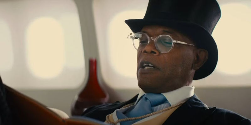 Richmond Valentine (Samuel L. Jackson) wearing a top hat and reading a paper in Kingsman The Secret Service.