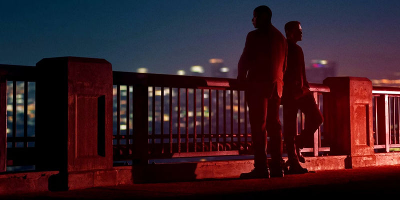 Deacon (Denzel Washington) and Baxter (Rami Malek) leaning against a railing bathed in red light in The Little Things