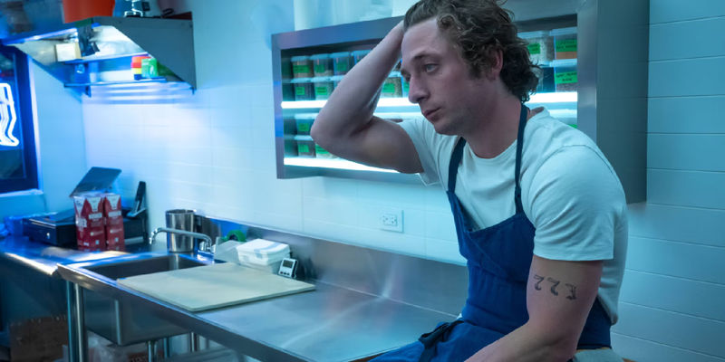 Carmy (Jeremy Allen White) pushes his hair back while sitting on the counter in the restaurant kitchen in The Bear's season 2 finale.