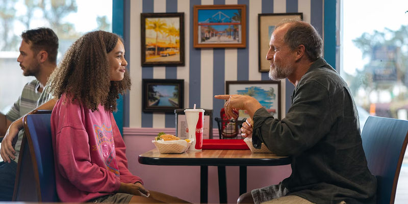 Doris (Nico Parker) and Paul (Woody Harrelson) eating burgers at a diner in Suncoast