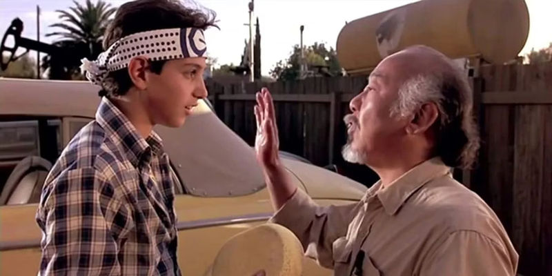Mr. Miyagi (Pat Morita) talking to Daniel (Ralph Macchio) in front of a car in The Karate Kid