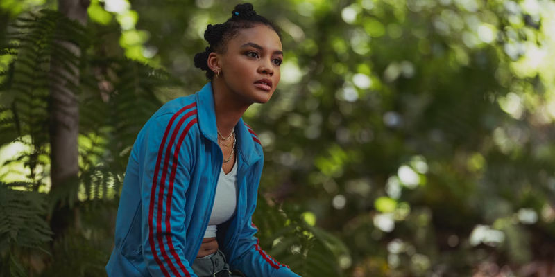 Mattie sits on a tree stump in the forest in Madame Web