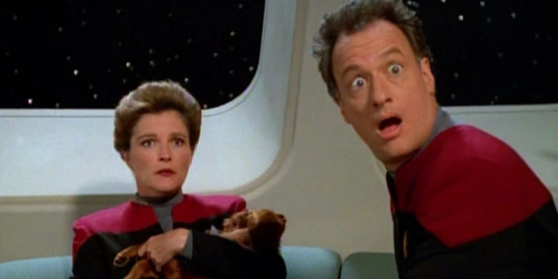 Captain Janeway holds a puppy as she and Q both look at something in surprise off-screen in the Star Trek: Voyager episode 