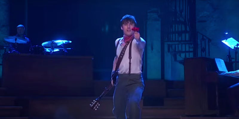 Orpheus holds out a red rose in Hadestown.