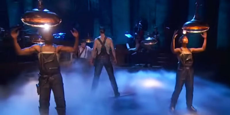 Orpheus stands between miners hold lamps in Hadestown