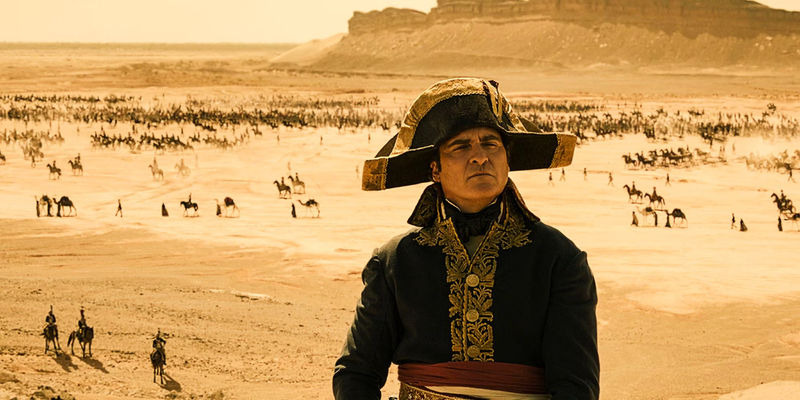 Joaquin Phoenix as Napoleon standing over a desert battlefield full of men, horses, and camels, in Ridley Scott's Napoleon