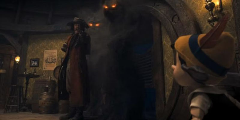 The Coachman (Luke Evans) standing with smoky monsters as Pinocchio looks on.