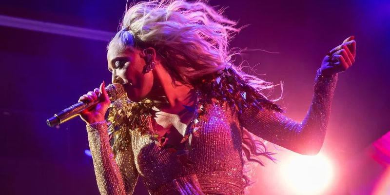 The Real Housewives of Beverly Hills star Erika Jayne sings on stage holding microphone in glamourous outfit and hairdo.