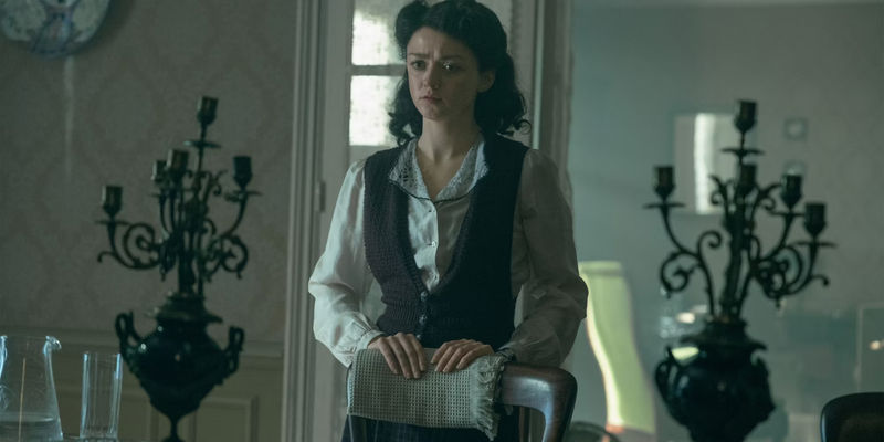 Maisie Williams As Catherine Dior Standing Behind A Chair In The New Look