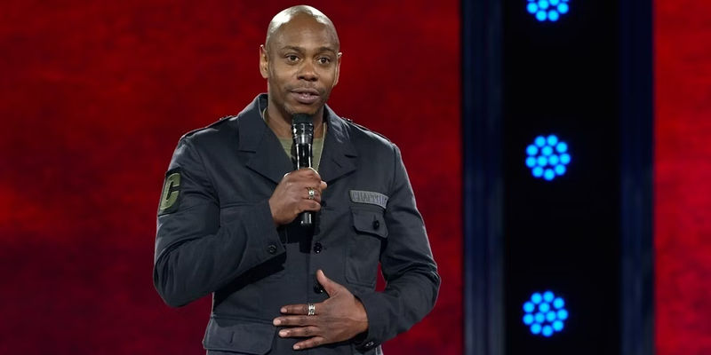 Dave Chappelle holding a mic and standing on stage.