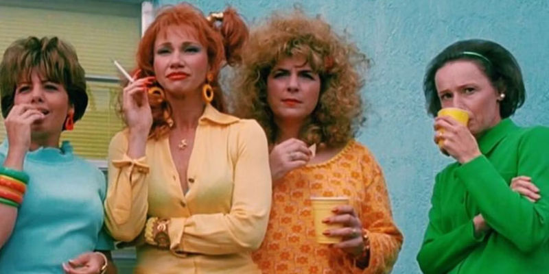 Joyce and another group of women stand against a wall and gossip about Edward while smoking and drinking in Edward Scissorhands