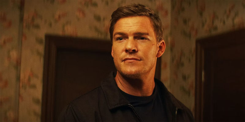 Alan Ritchson smirking as Jack Reacher in the Prime Video show Reacher