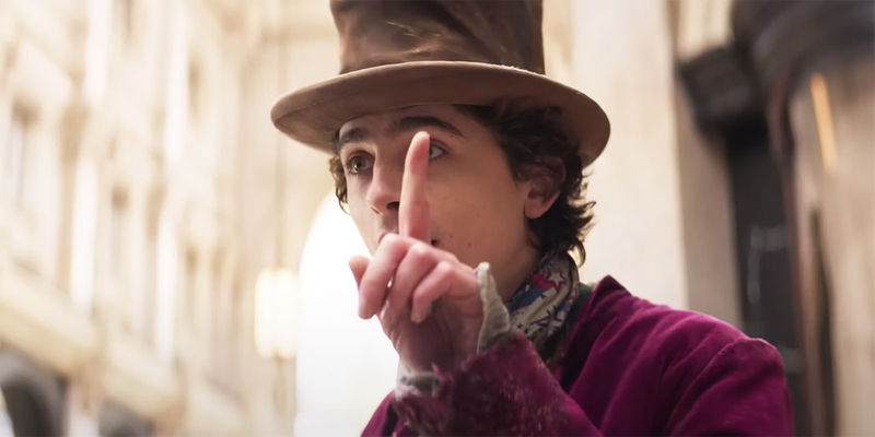 Timothee Chalamet as Willy Wonka holding his index finger up.