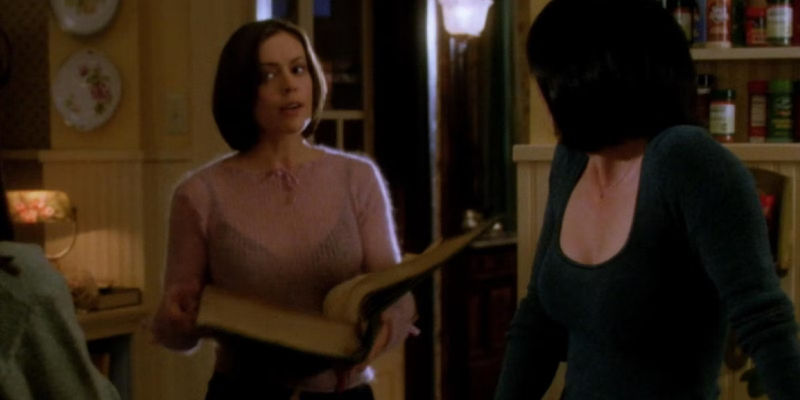Prue looks over at Pheobe who's holding the Book of Shadows open in Charmed season 1.