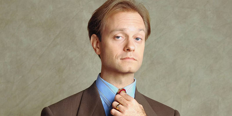 David Hyde Pierce as Niles Crane adjusts his tie while looking at the camera in Frasier.