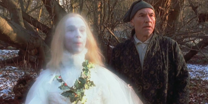 Patrick Stewart as Ebenezer Scrooge in his robe and pyjamas standing in the woods with the Ghost of Christmas Past