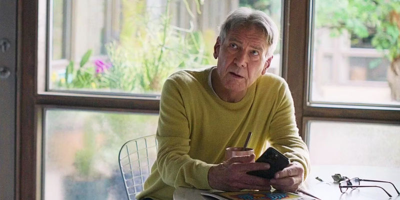 Harrison Ford sitting at a table with his cell phone in Shrinking