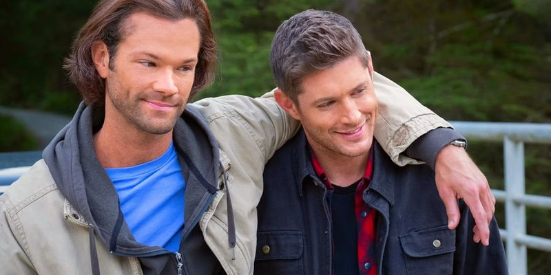 Jared Padelecki as Sam Winchester and Jensen Ackles as Dean Winchester smiling while standing in the forest in Supernatural's final episode