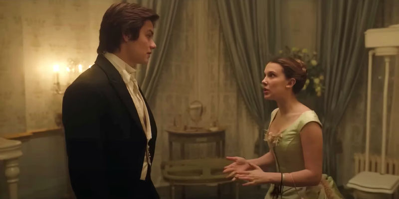 Enola Holmes (Millie Bobby Brown) and Tewkesbury (Louis Partridge) in ball outfits looking at each other