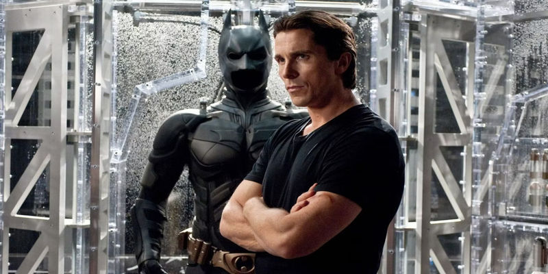 Christian Bale as Bruce Wayne standing in front of his Batman suit in The Dark Knight