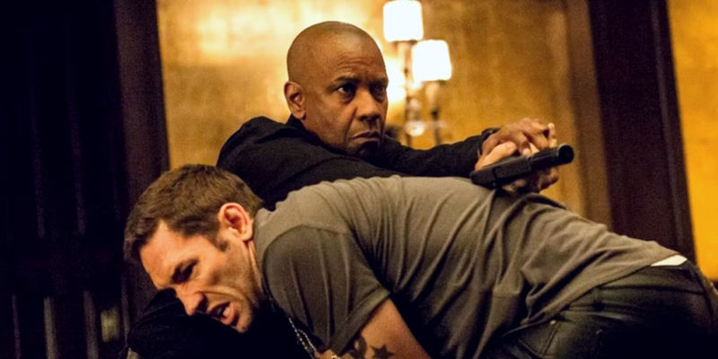 Denzel Washington as Robert McCall shoots a pistol over a henchman in The Equalizer.
