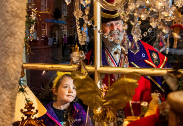 Town cryer and little girl looking through a christmas window