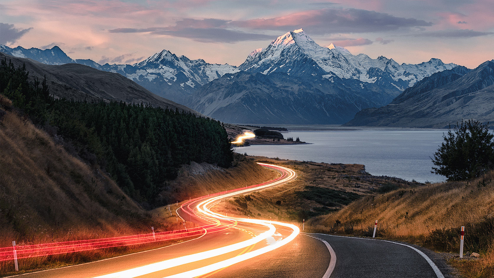 New Zealand alpine landscape with a winding road, lake and snow-capped mountains