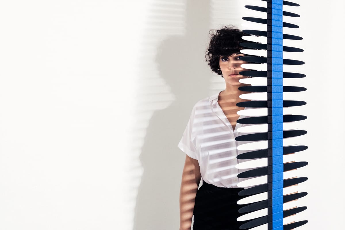 Marion Rampal dans un décor blanc légèrement cachée par une sculpture ajouré bleue et blanche.