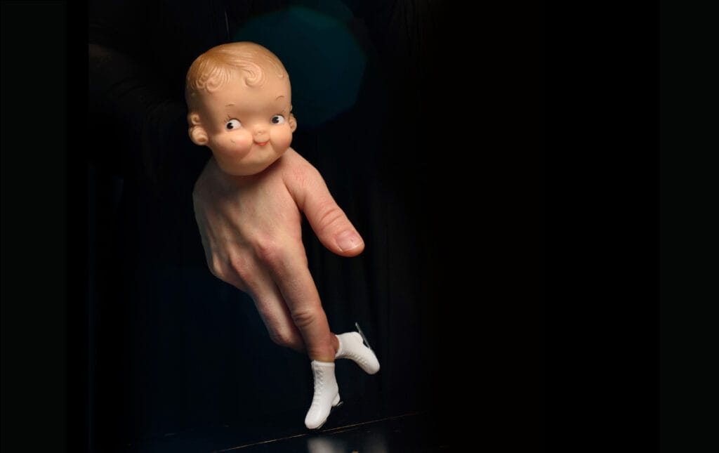 Une main nue vers le bas et mini patins à glace sur les doigts avec une tête de poupée qui composent une marionnette.