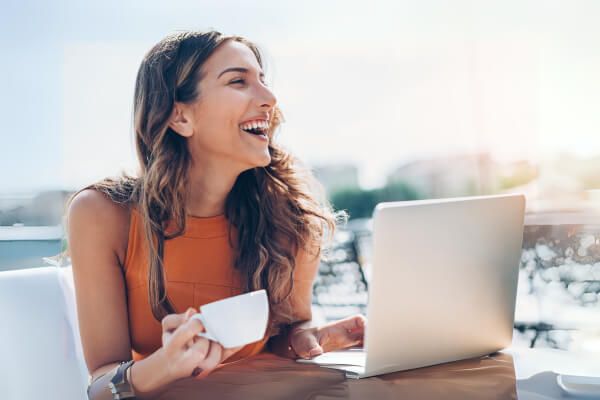 A woman holding a cup while working on her laptop