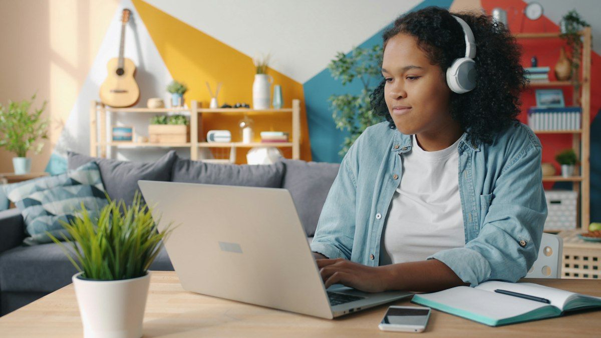 Teenager wearing headphones working on a laptop at home