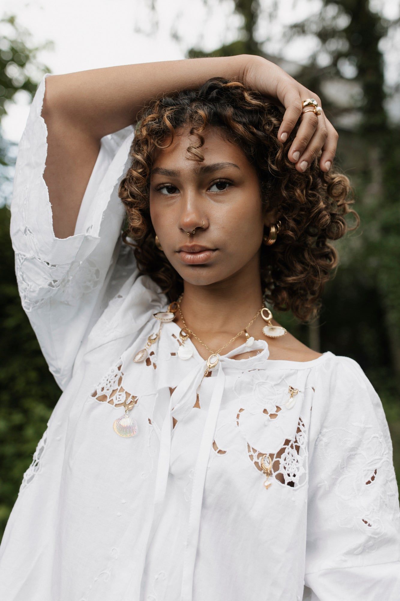 A woman with curly hair poses outdoors, one arm raised, wearing the WALD Berlin x Helena Harfst Necklace Blouse by WALD Berlin.
